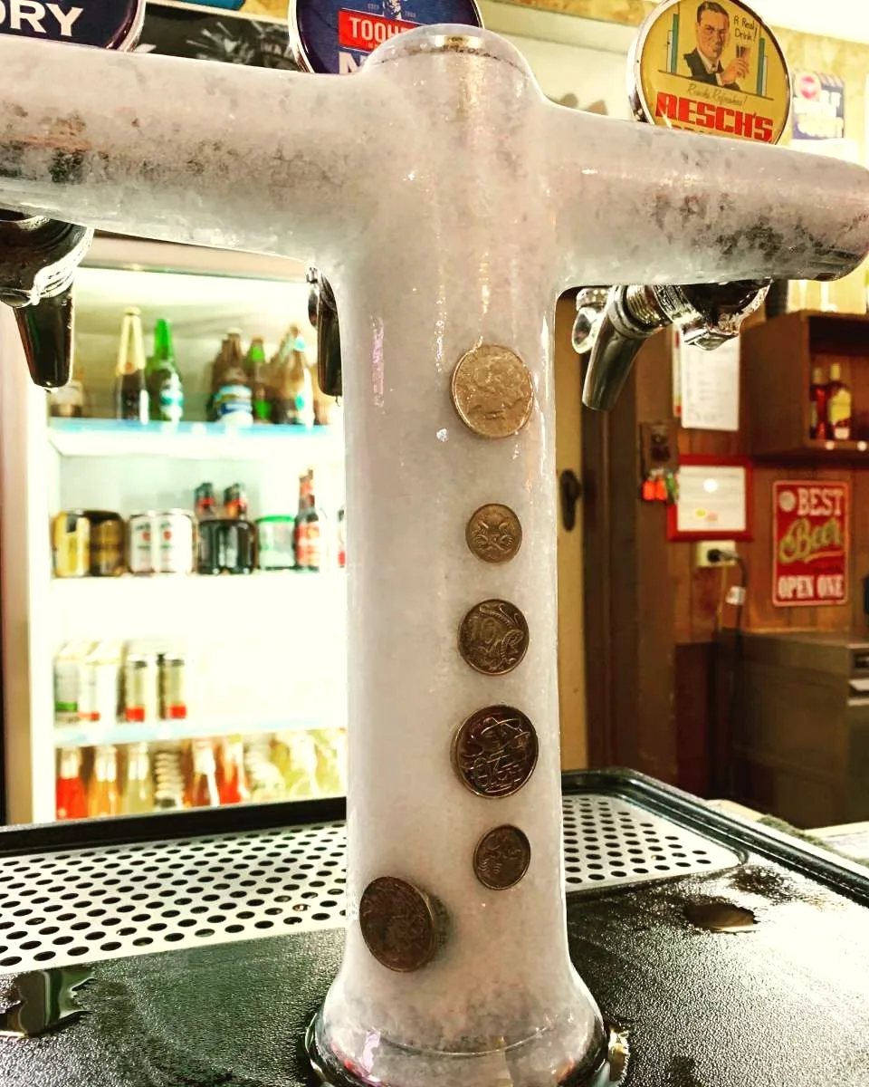 A frosted beer tap on the bar with coins stuck to the ice on it.